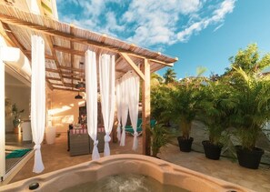 A spa area with a hot tub, white curtains, and potted plants.