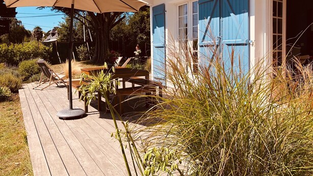 A wooden deck with outdoor furniture, a large umbrella, and a building with blue shutters.