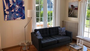 A living room with a dark grey sofa, a glass coffee table, a floor lamp, and a painting on the wall.