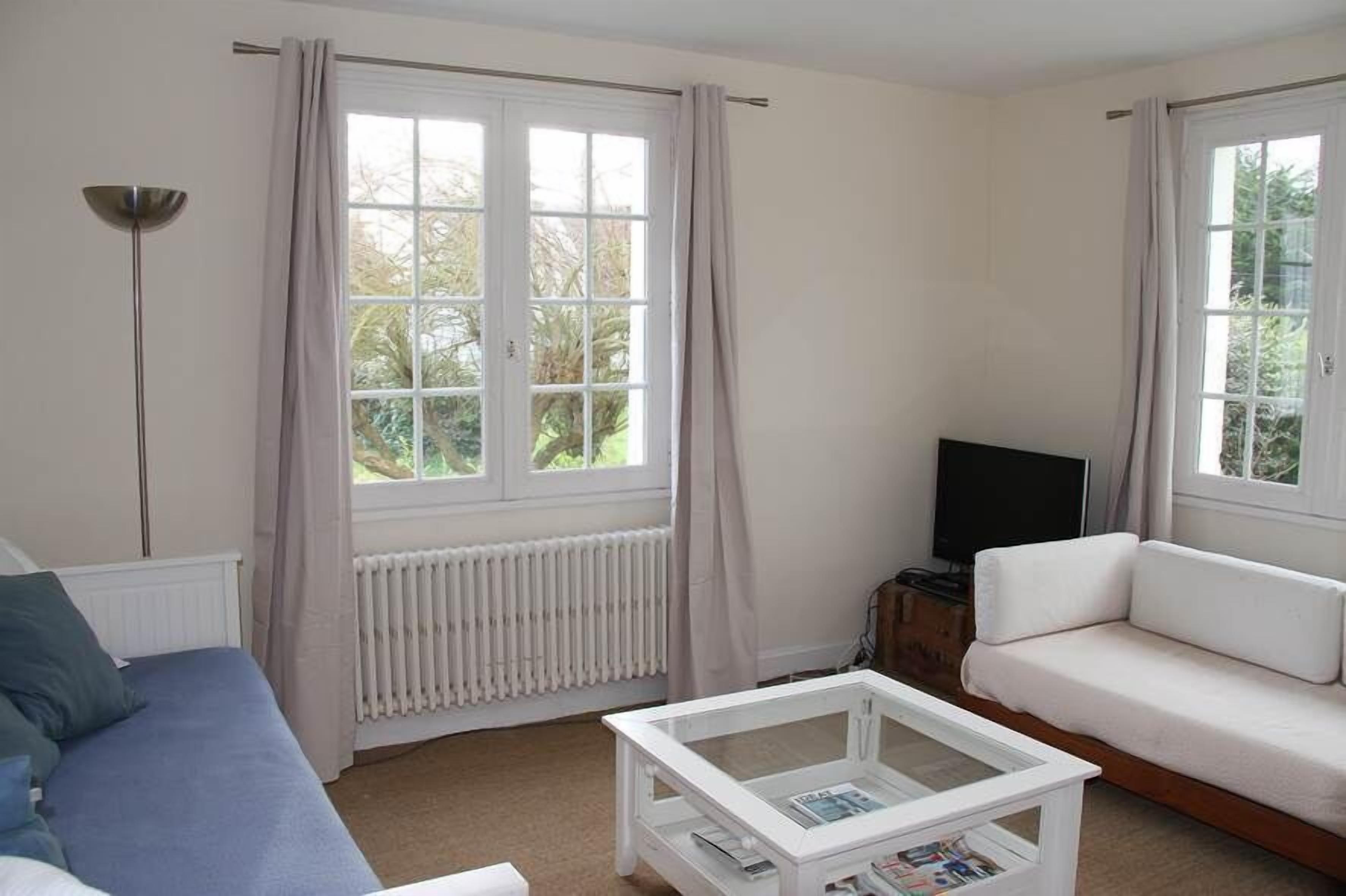 A living room with a sofa, a coffee table, a TV, and large windows with curtains.