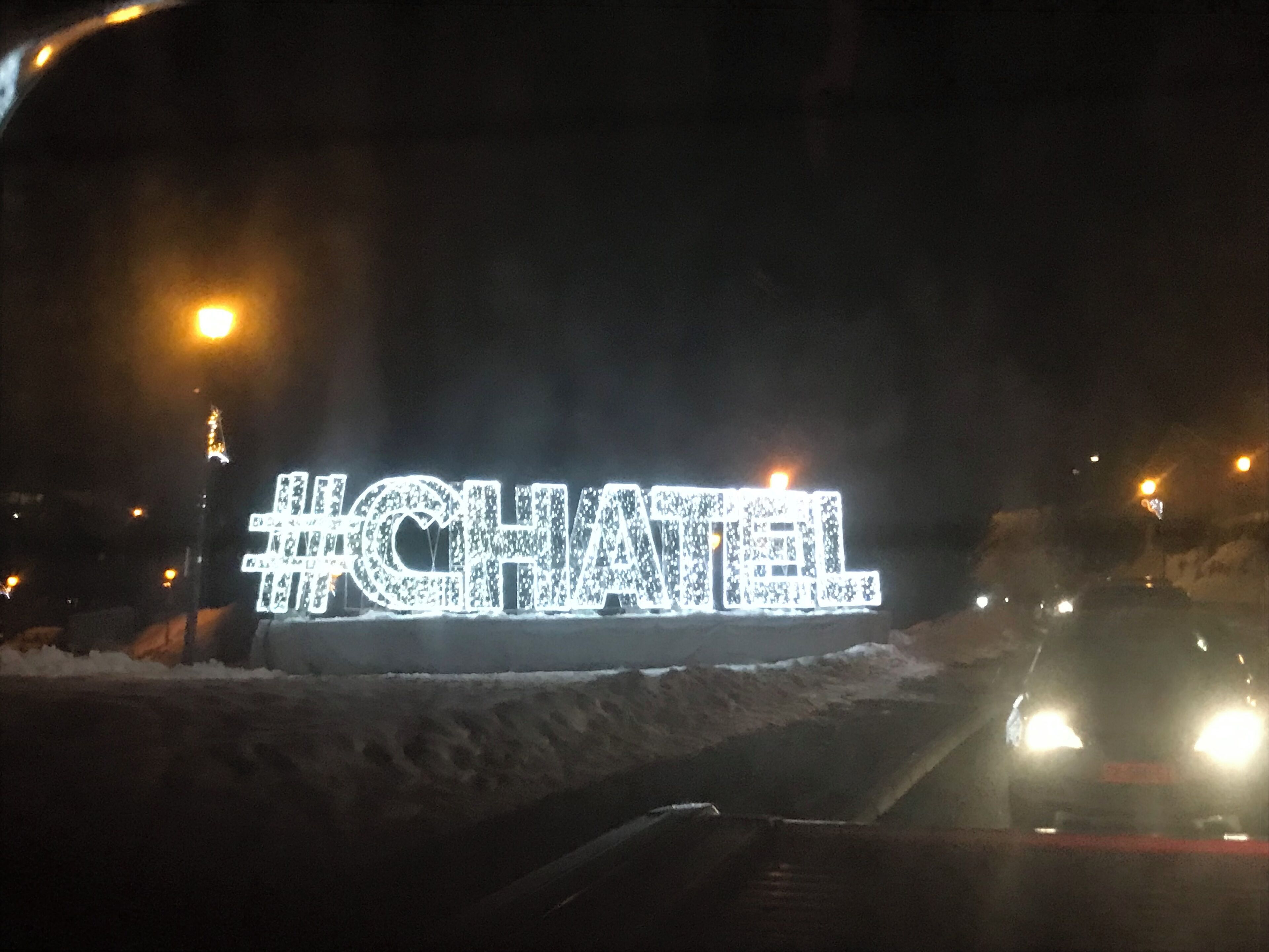 A #CHANEL sign illuminated in white lights on a snowy road at night.