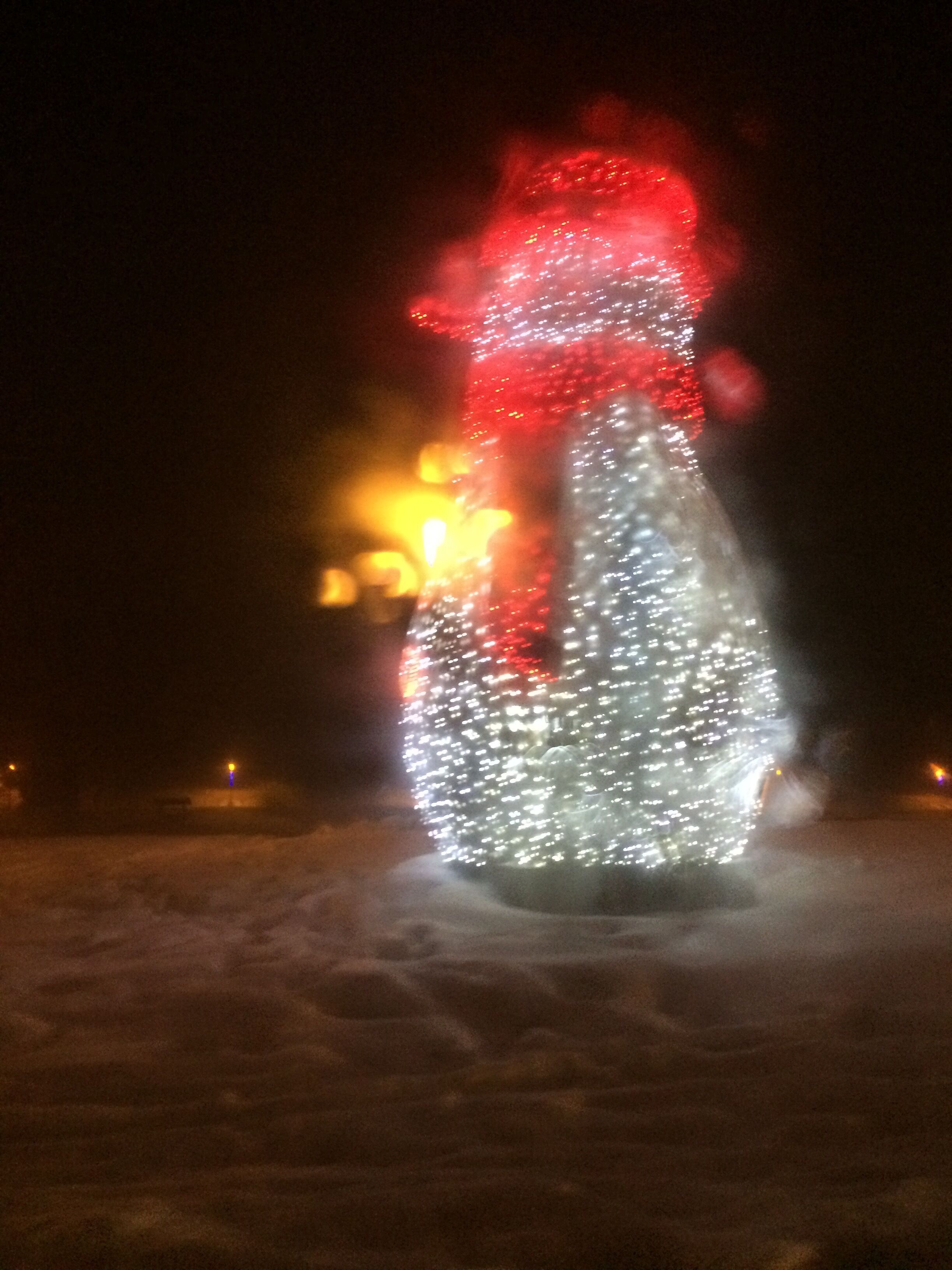 A snowman with a red hat and a bottle, illuminated by lights.