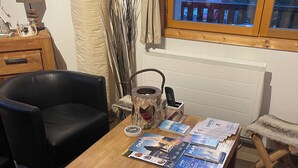 A wooden dining table with a magazine and a kettle. There is a black chair and a fur chair. A window shows a building outside.