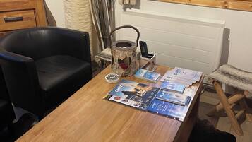 Un tavolo da pranzo in legno con una rivista e un bollitore. Si nota una sedia nera e una poltrona in pelliccia. Da una finestra si vede un edificio all'esterno.