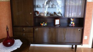 A wooden cabinet with glass doors, a red vase, and a small clock.
