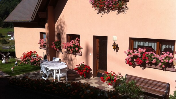 A building with a checkered floor, a table with chairs, and hanging flower baskets.