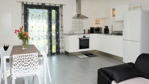 A modern kitchen with white cabinets, a Bosch refrigerator, a microwave, and a stove. There is a dining table with a vase of flowers and a chair. - Apartments in an old renovated sheepfold  (Figari)