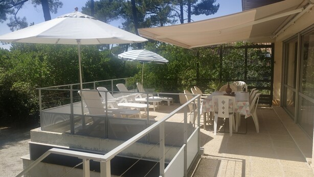 Eine Terrasse im Freien mit Glastischen und -stühlen, umgeben von Bäumen und beschattet durch Sonnenschirme.