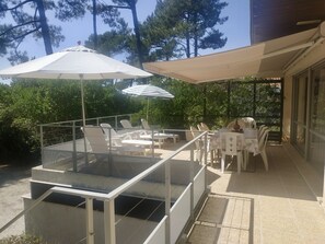 Eine Terrasse im Freien mit Glastischen und -stühlen, umgeben von Bäumen und beschattet durch Sonnenschirme.