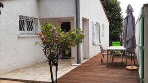 A covered outdoor area with a wooden deck, a table with chairs, and a green chair.