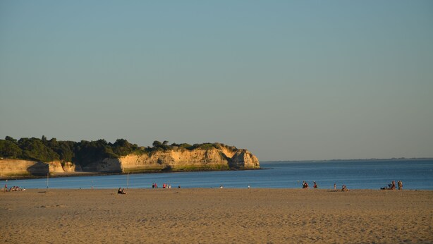 A beach with people relaxing, a sandy shore, and cliffs in the background.