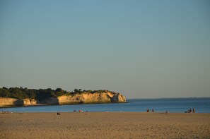 Ein Strand mit Menschen, die entspannen, ein sandiger Uferstreifen und Klippen im Hintergrund.