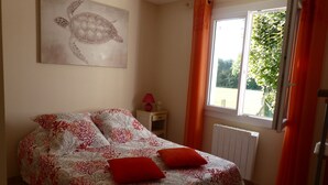A bedroom with a bed, a window with curtains, a radiator, and a wall painting.