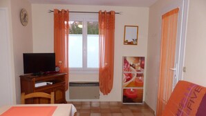 A room with a bed, a desk with a TV, a window with curtains, a radiator, and a sofa.