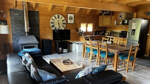 Ein gemütliches Wohnzimmer mit Kamin, einer großen Uhr, einem Fernseher und einem Essbereich mit Holztischen und -stühlen.