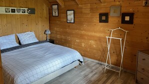 Ein Schlafzimmer einer Holzhütte mit Bett, Nachttisch, Kommode und Bilderrahmen an der Wand.
