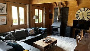 Ein gemütliches Blockhaus-Interieur mit einer Couch, einem Holztisch, einem Kamin und einer großen Wanduhr.