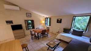 A compact room with a bed, a dining table with chairs, a TV, and a window with a view of greenery. - Mas Cevenol with pool in Gagnieres (Gagnières)