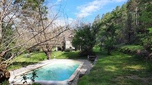 A rectangular swimming pool with a stone border, surrounded by a grassy area and trees. - Mas Cevenol with pool in Gagnieres (Gagnières)
