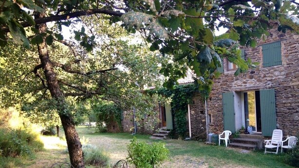 A stone building with a covered porch, a table with chairs, and a tree in the foreground. - Mas Cevenol with pool in Gagnieres (Gagnières)
