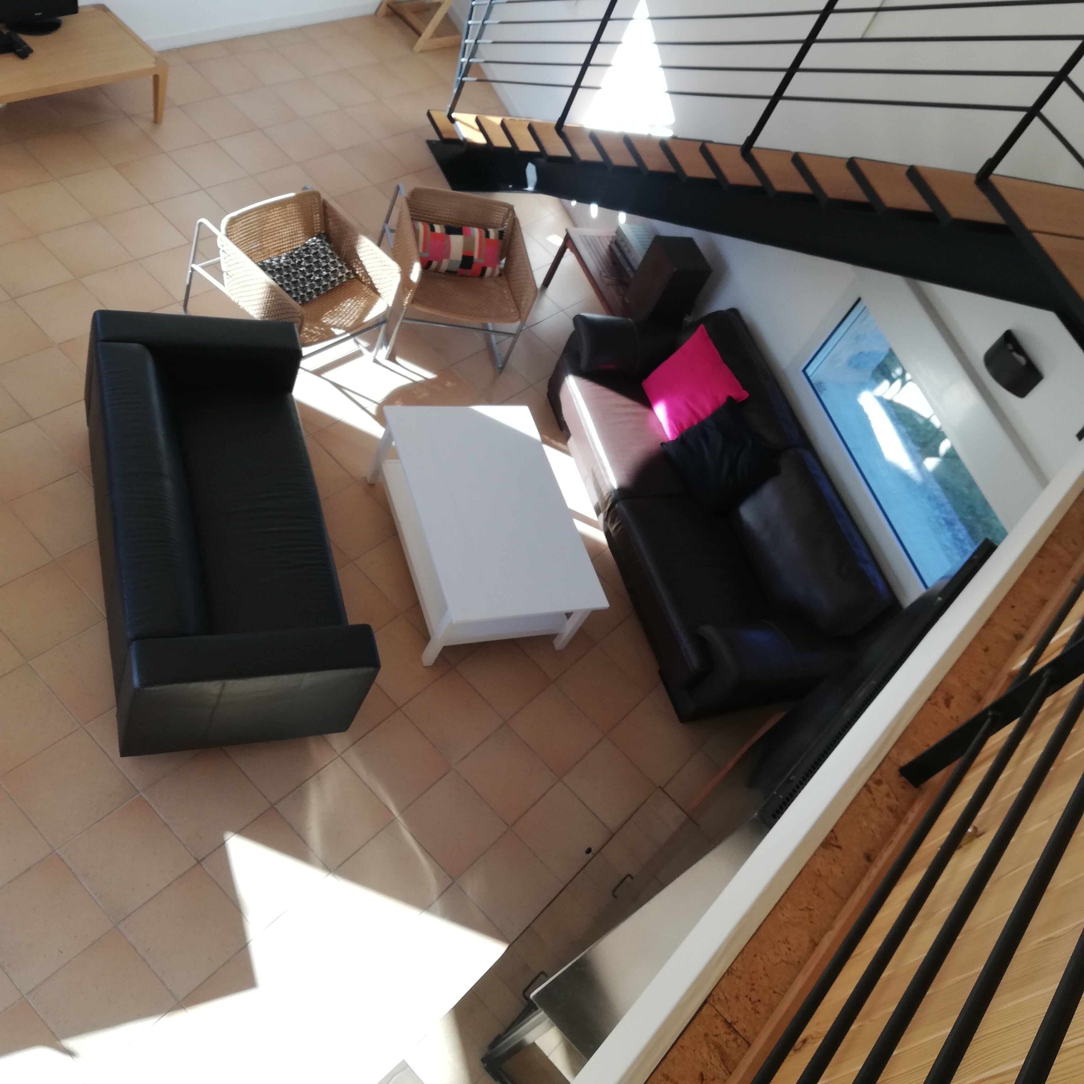 Een moderne woonkamer met een zwarte bank, een witte salontafel en een televisie. Er is een trap die naar een hoger niveau leidt.
