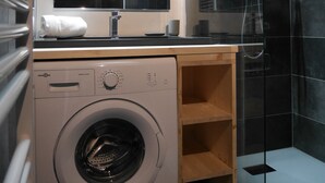 Pequeña área de lavado con lavadora, un lavabo y una ducha.