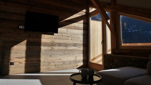 Una habitación acogedora con paredes de madera, un televisor de pantalla plana montado en la pared, una chimenea de piedra y un amplio ventanal con vistas al exterior.
