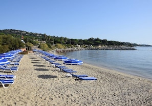 A beach with rows of blue sun loungers and umbrellas, a rocky breakwater, and a clear view of the water. - Large villa with pool and view to the sea in Sainte-Maxime - Beauvallon (Grimaud)