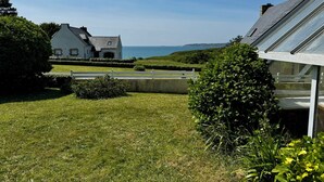 A house with a view of the sea, a white fence, and well-maintained grass.