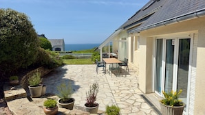 A stone patio with a table and chairs, potted plants, and a view of the sea.