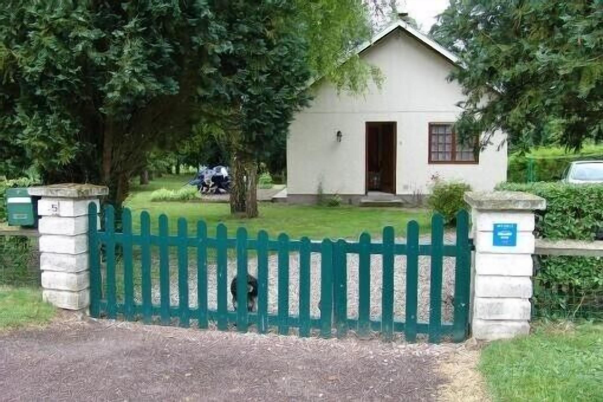 A small, white building with a green picket fence in front, surrounded by trees.