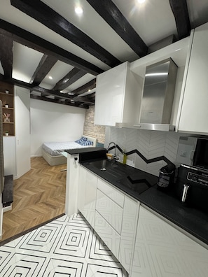 A modern kitchen with white cabinets, a black countertop, and a herringbone-patterned floor. - Private terrace, AC & quiet in the Latin Quarter (Paris)