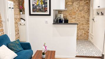 A modern living room with a blue sofa, a wooden coffee table, and a kitchen area with stone walls and wooden beams.