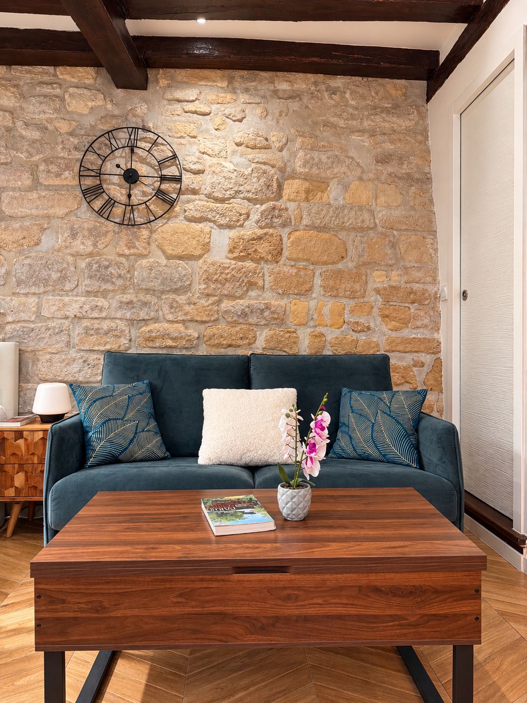 Ein Wohnzimmer mit einer Steinsäule, einem dunkelblauen Sofa, einem Holztisch und einer Wanduhr.