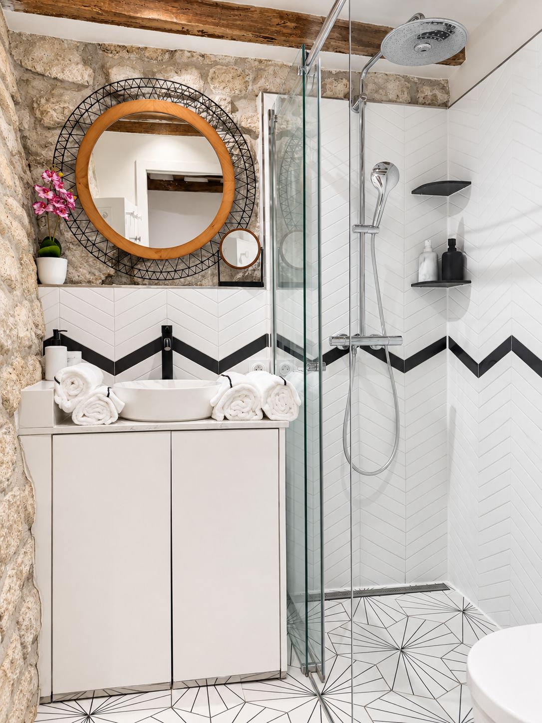 Un baño moderno con ducha envuelta en vidrio, un lavabo blanco sobre encimera negra y un espejo con marco de madera.