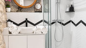 Un baño moderno con ducha envuelta en vidrio, un lavabo blanco sobre encimera negra y un espejo con marco de madera.