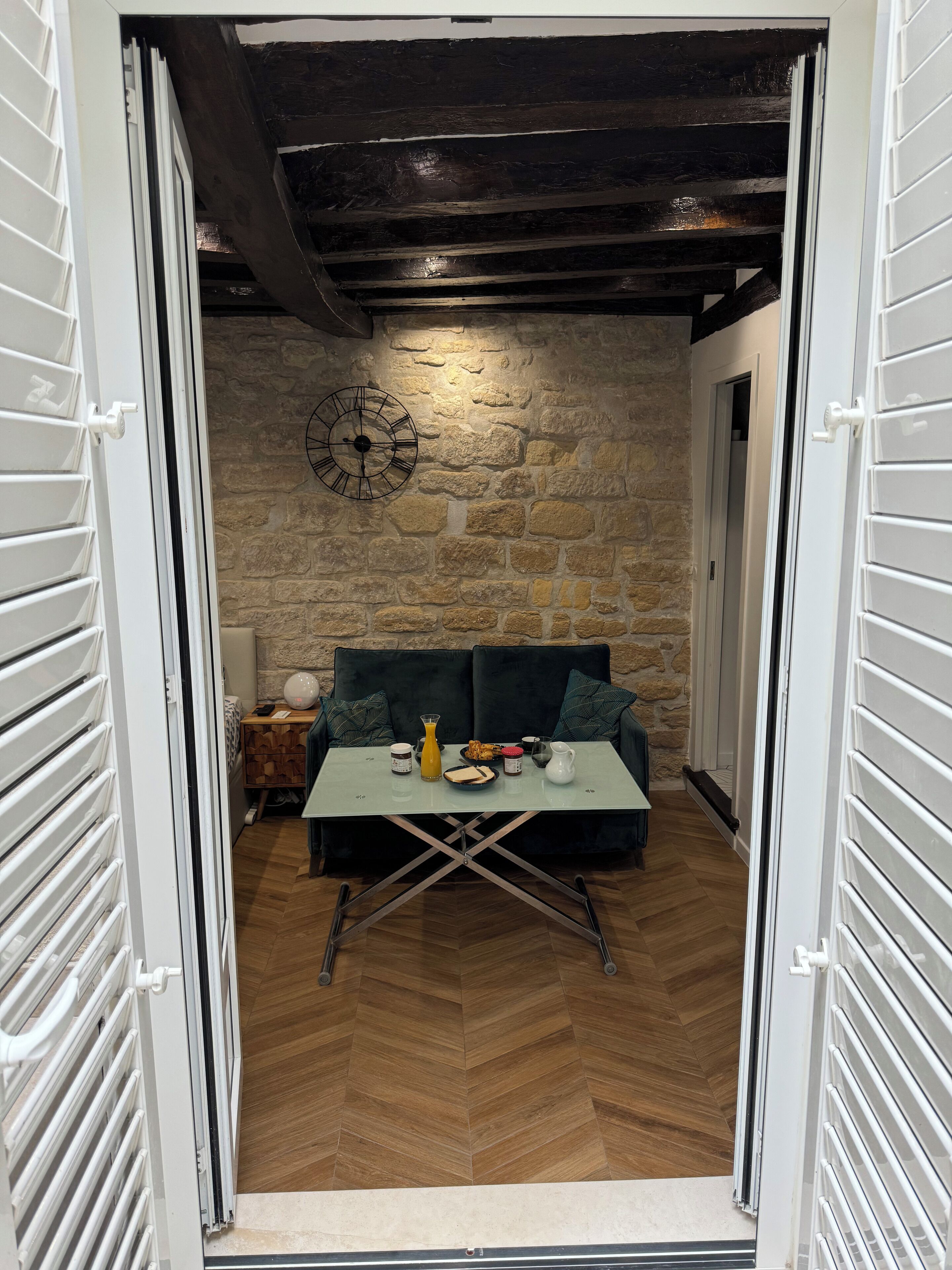 Une pièce chaleureuse avec un mur en pierre, une horloge, une table ornée d’un vase et un canapé.