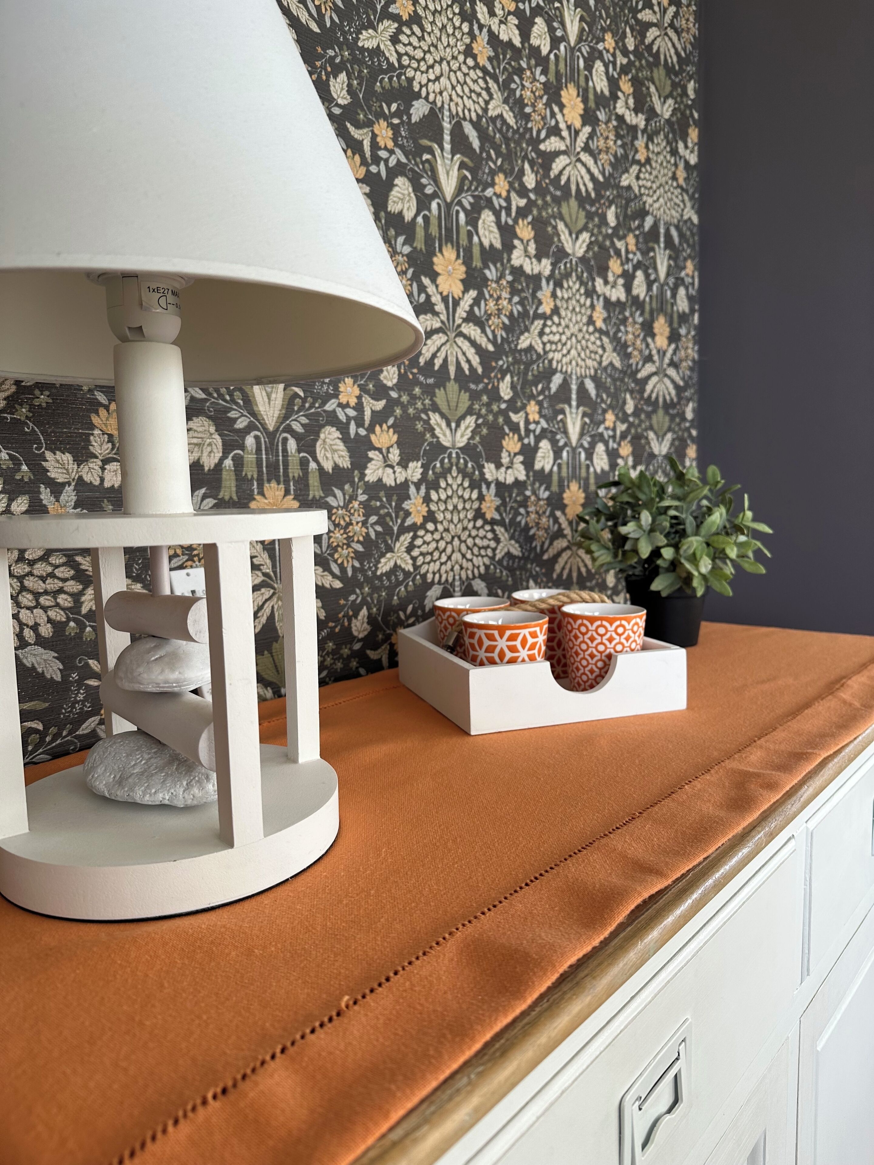 A white lamp on a white stand with a patterned wallpaper background.