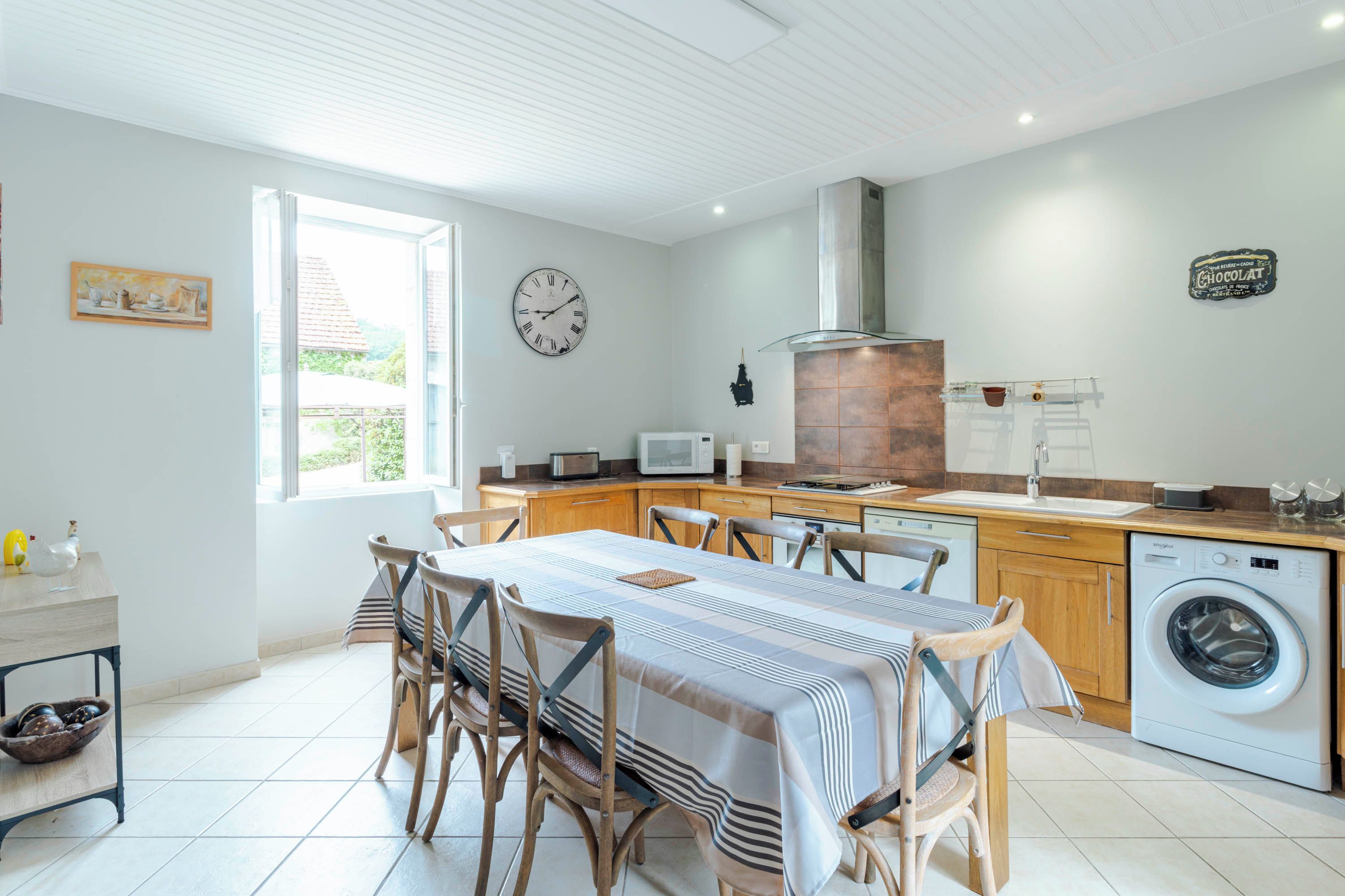Une cuisine moderne avec un coin repas, un lave-linge et une horloge au mur.
