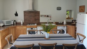 A kitchen with wooden cabinets, a gas stove, a microwave, a sink, and a dining table with chairs. - Beautiful view of the countryside house 8 pers pool Wifi near Sarlat (Salviac)