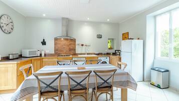 A modern kitchen with a central island, wooden chairs, a dining table, and a large window.