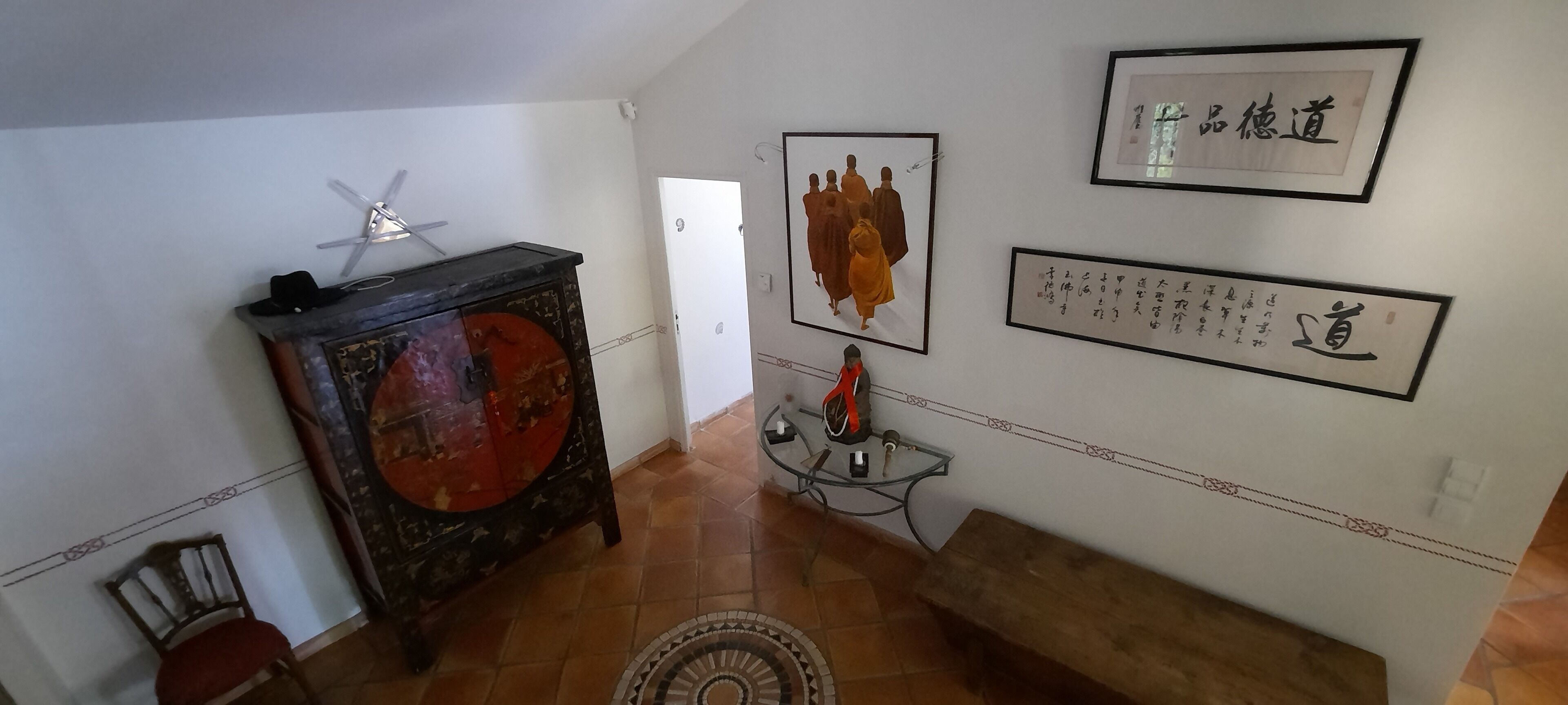 A hallway with a wooden cabinet, a chair, a small table with a vase, and framed calligraphy on the walls.