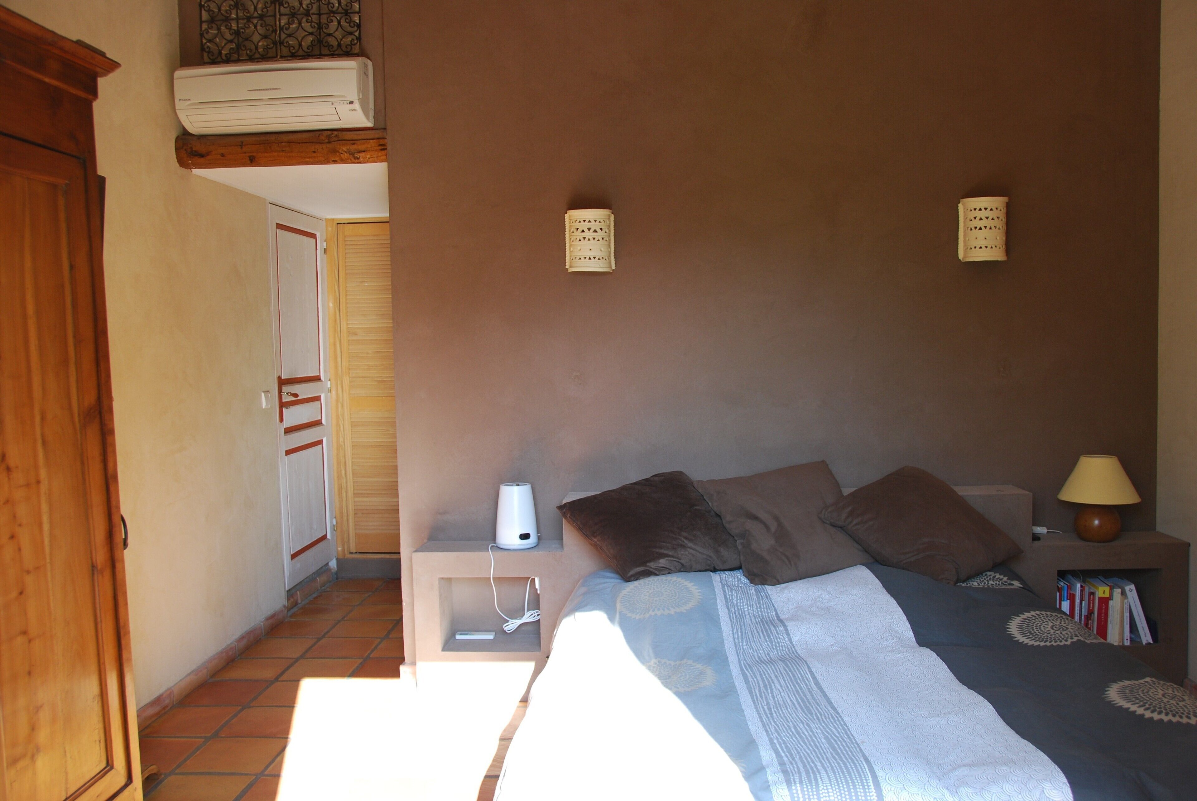 Quarto com cama, mesas de cabeceira, ar condicionado fixado na parede e luminária.