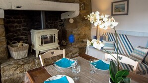 Una chimenea de piedra con una estufa blanca, una mesa de comedor con servilletas y platos azules, y un sofá a rayas con almohadones.