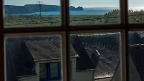 Vista a través de una ventana mostrando un paisaje costero con cielo despejado, un promontorio rocoso distante y una masa de agua.