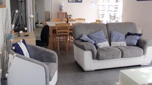 Ein Wohnzimmer mit grauem Sofa, einem Esstisch und Stühlen. Auf dem Tisch steht ein Blumentopf.