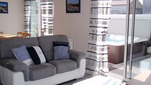 Ein Wohnzimmer mit grauem Sofa, gestreifteren Kissen, einer Glastür, die auf einen Balkon führt, und einem Whirlpool.