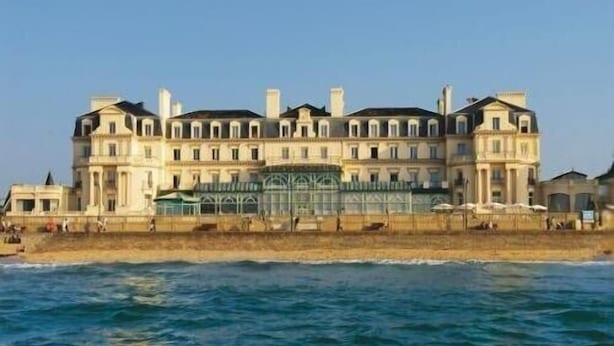 Un grand hôtel à plusieurs étages, doté d’une façade symétrique, situé juste à côté d’une plage.