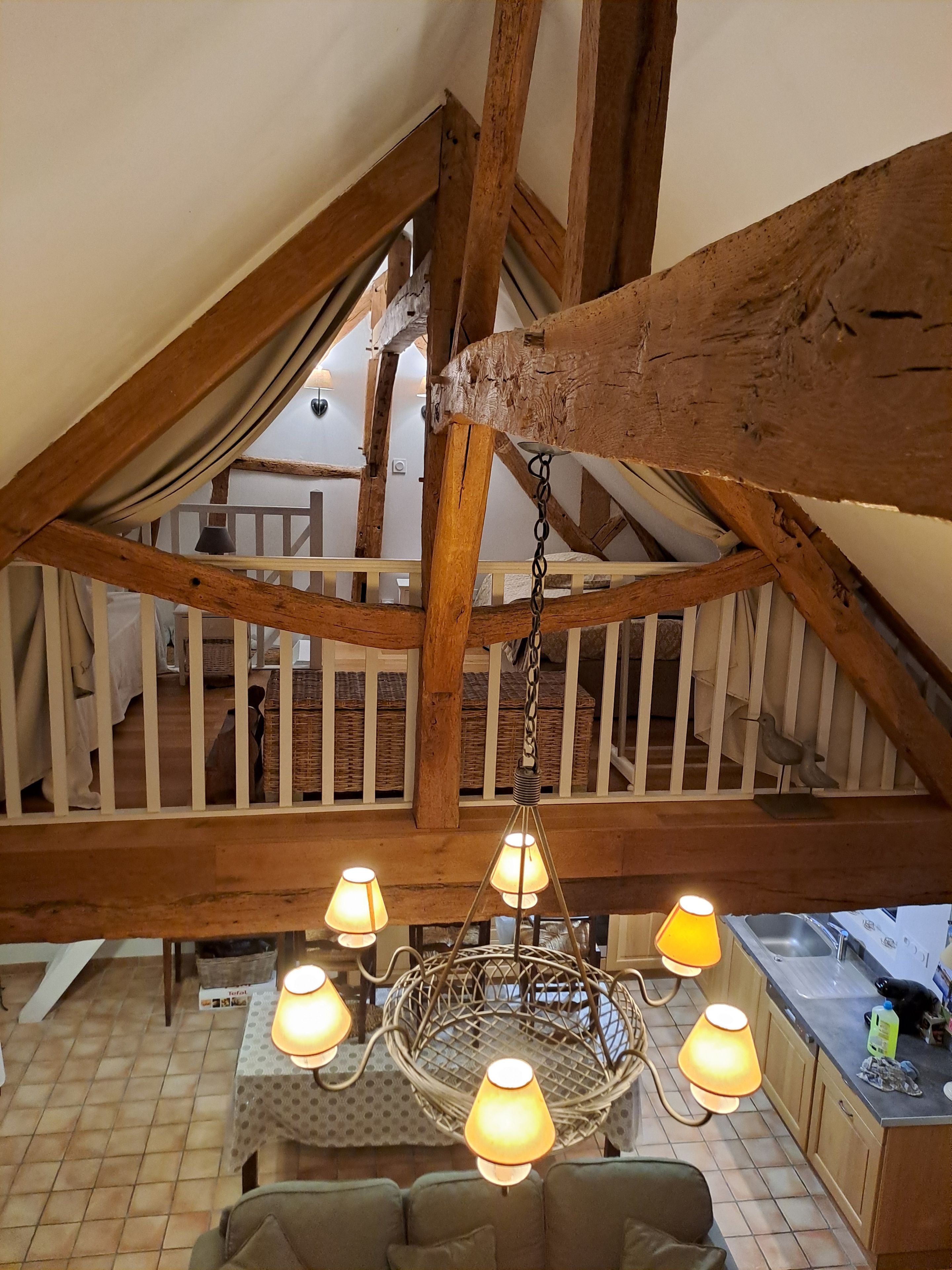 Une pièce de style « loft », avec des poutres en bois apparentes, un luminaire suspendu et une vue sur un balcon.