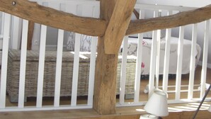 Ein Zimmer mit freiliegenden Holzbalken, einem weißen Babybett und einem Korbwäschekorb.